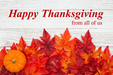 Happy Thanksgiving greeting with red and orange fall leaves and a pumpkins on weathered wood