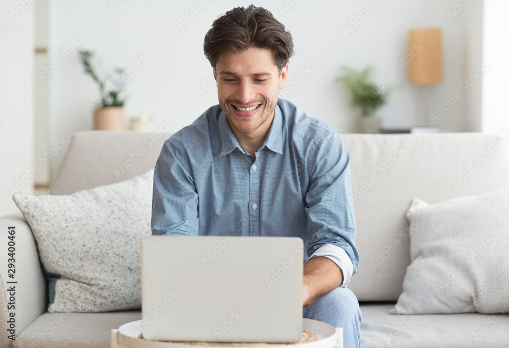 Smiling Man Working On Laptop Sitting On Sofa At Home Smiling Man Working On Laptop Sitting On Sofa At Home