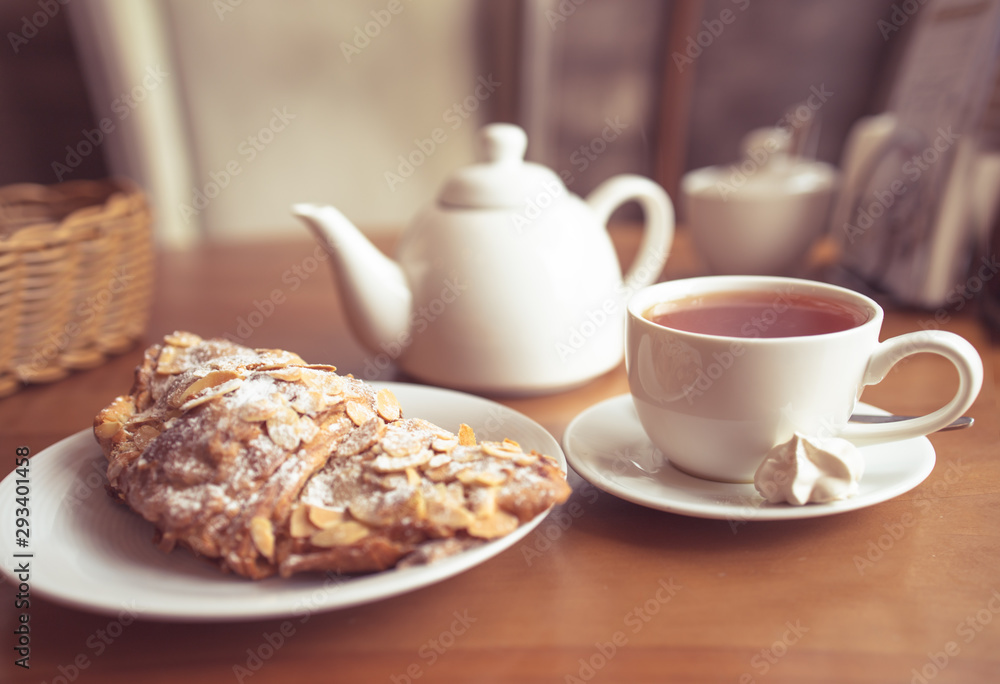 Tea cup, teapot and croissant on table in cafe Tea cup, teapot and croissant on table in cafe