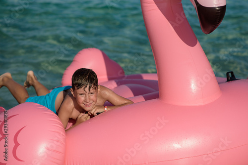 Obraz na płótnie Cute European boy laying on huge inflatable pink flamingo in sea, he enjoying his vacations and smiling to camera. w salonie