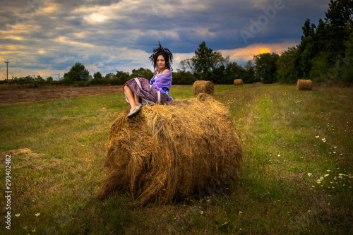Woman on a meadow with hay bale at sunset