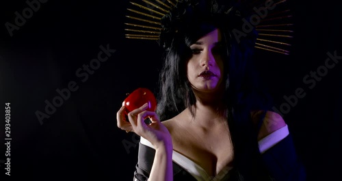A nightmarish carnival image of a woman in the dark with a crown of shims and a large poisoned red Apple