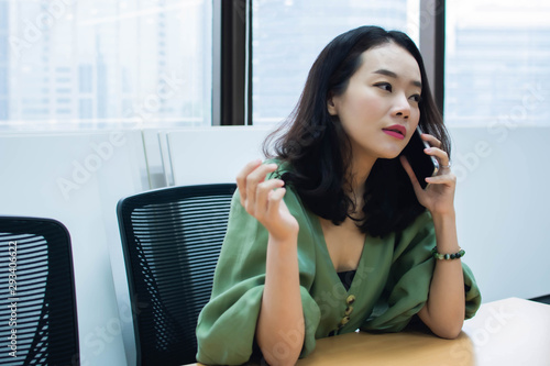 An asian beautiful business woman is happily talking on her mobile phone in working place
