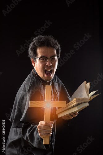 Dark tone, rim light - Priest show crucifix while holding bible  to exorcise ghost on black background
