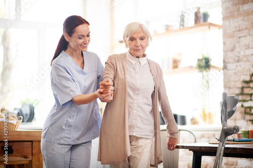 Aged woman walking after surgery with the help of nurse