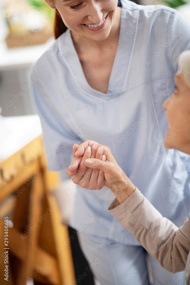 Thankful aged woman shaking hand of caregiver