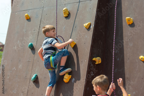 A boy in climbing equipment conquers the top of an artificial tower for climbers in a sports extreme recreation park.