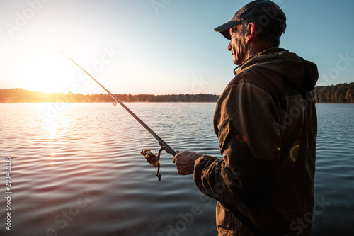 Male fisherman at dawn on the lake catches a fishing rod. Fishing hobby vacation concept. Copy space.