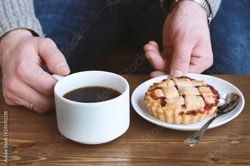 man in grey sweater drinks black lungo americano coffee in winter autumn in coffee shop eating classic american home-made cherry pie on white plate on wooden table. Fall mood instagram style