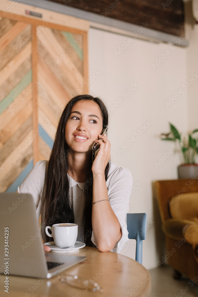 Young businesswoman with laptop talking on the phone at table in a cafe Young businesswoman with laptop talking on the phone at table in a cafe