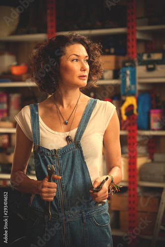 car mechanic woman in blue overalls with a wrench in her hand in the car repair shop. beautiful middle-aged woman with tools to repair the car in the garage. instagram image filter retro style