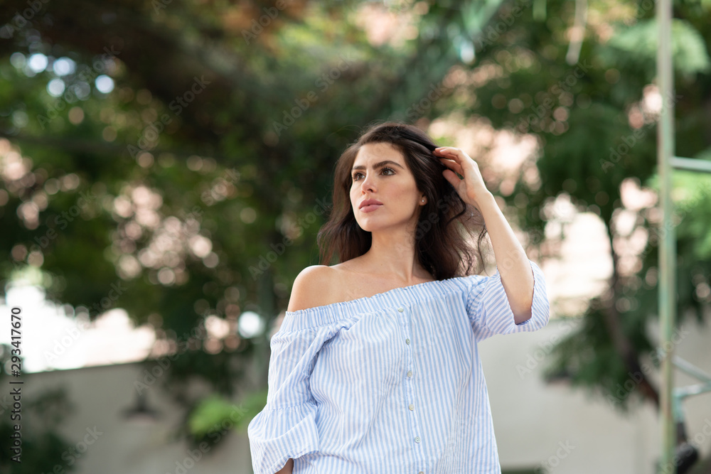 A portrait of a lovely romantic young woman outdoors, touching her hair