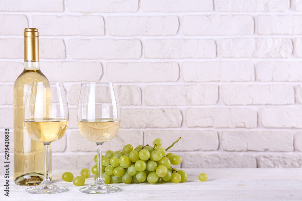 Obraz premium Vintage bottle of white wine without label, two glasses and bunch of grapes on wooden table, lofty white brick wall background. Expensive bottle of chardonnay concept. concept. Copy space.