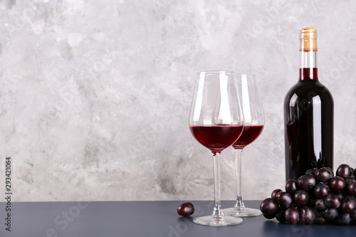 Vintage bottle of red wine without label, two glasses and bunch of grapes on wooden table, grunged concrete wall background. Expensive bottle of cabernet sauvignon concept. Copy space,