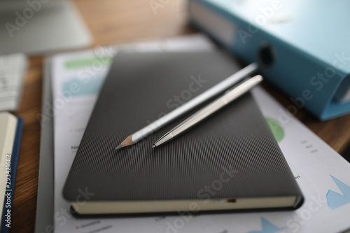 Diary with silver pen and pencil lie on wooden tabble in office background closeup. Business planning concept
