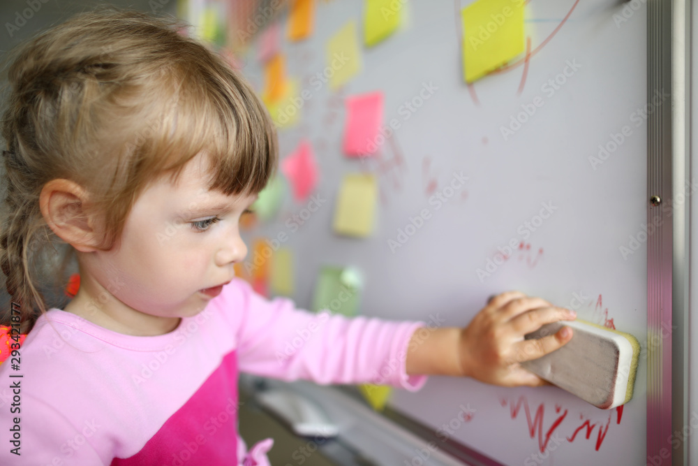 Portrait of smart small girl standing in modern classroom and holding special erasing marker utility to start lovely drawing again. Creative childhood concept