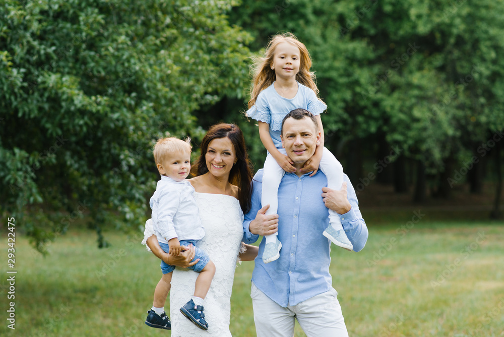 Portrait of a beautiful family: mom, dad, two-year-old son and five-year-old daughter. Parents hold children in their arms. The family is dressed in blue and white clothes Portrait of a beautiful family: mom, dad, two-year-old son and five-year-old daughter. Parents hold children in their arms. The family is dressed in blue and white clothes