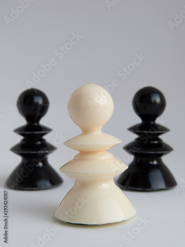 One white chess piece standing in front and two black pieces standing behind it on both sides