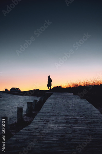 Silhouette of a girl in the evening sky walking on a wooden path after sunset. Walking home from the beach. Praia da Bordeira at the Algarve Coast in Portugal, Atlantic Ocean © Ricardo