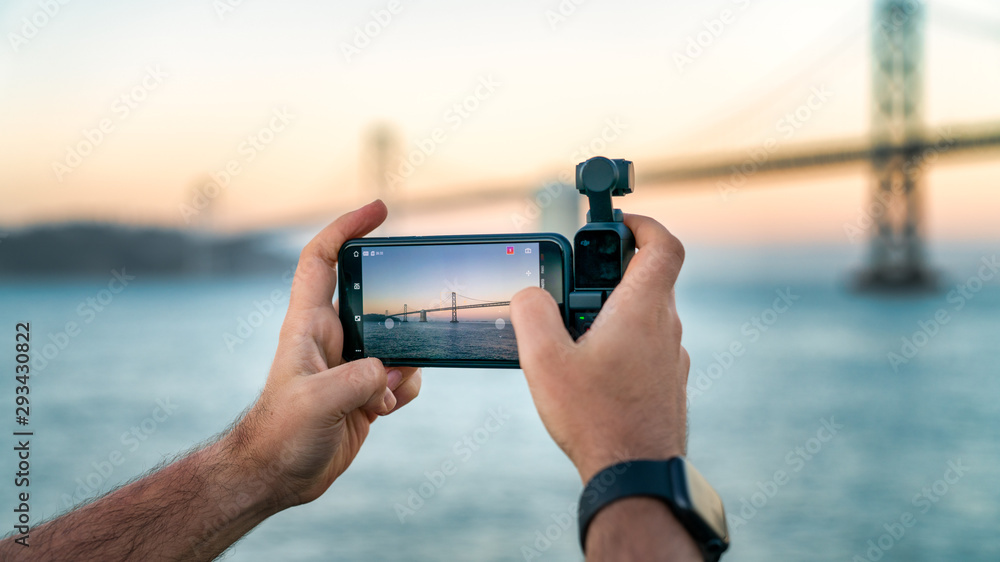 A photographer is using DJI Osmo Pocket to take footage of a Bay Bridge, San Francisco, USA