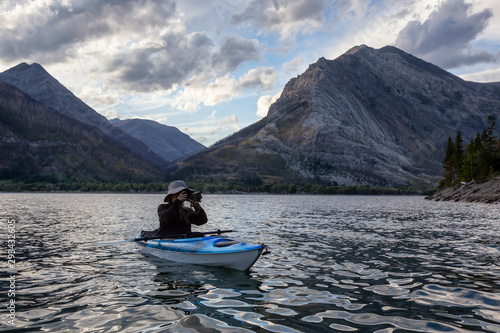 Adventurous Man Kayaking in Glacier Lake surrounded by the beautiful Canadian Rocky Mountains during a cloudy summer sunset. Taken in Upper Waterton Lake  Alberta  Canada.