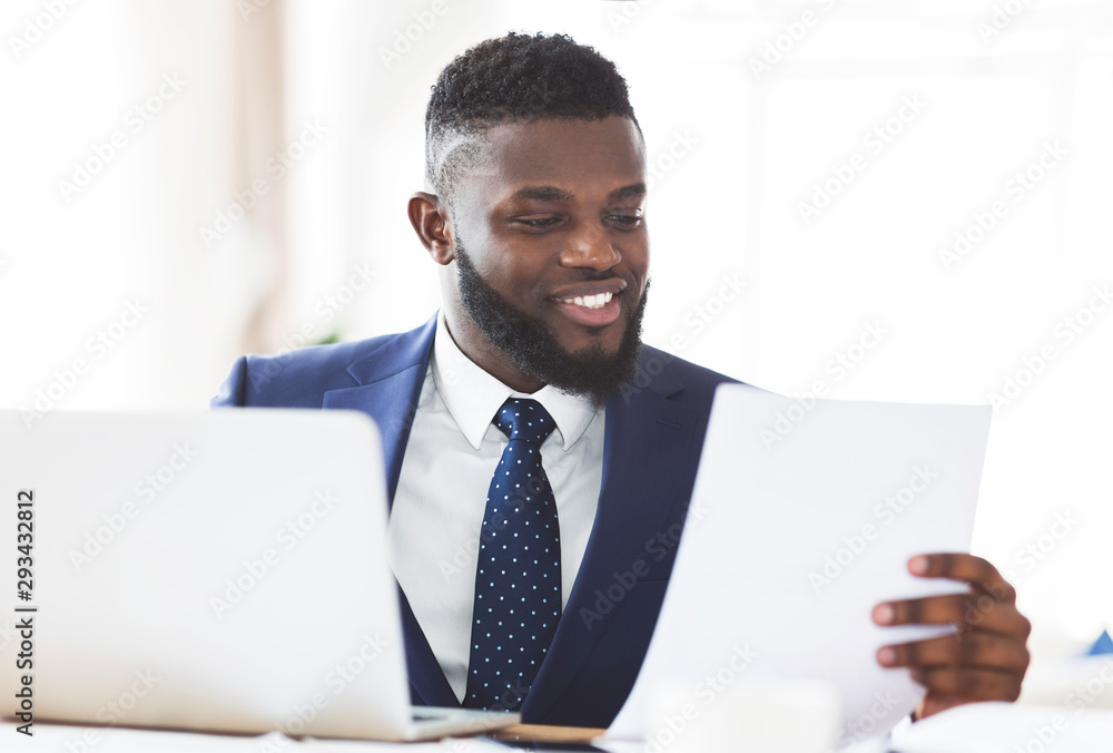 Smiling african american businessman checking reports in modern office