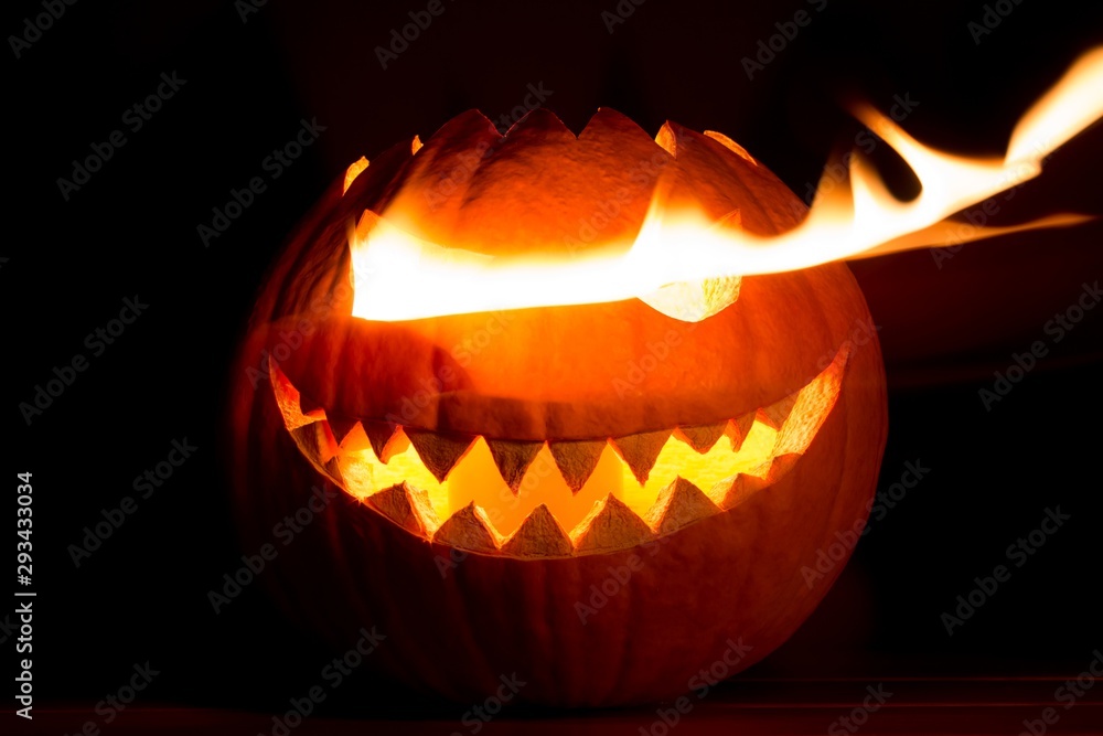 Fototapeta premium Spooky carved halloween pumpkin with glowing hot fire flame eyes. Big helloween autumn symbol with mad face, glowing eyes, mouth and teeth. Scary hot nightmare horror with evil smile at october 31st