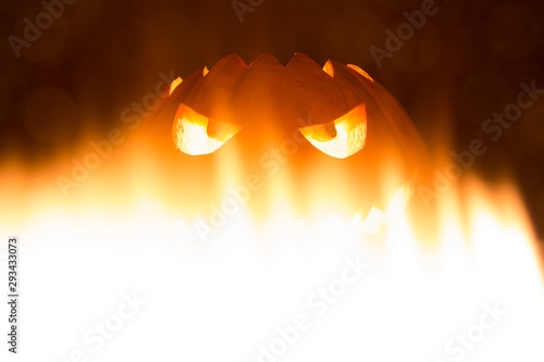 Spooky carved halloween pumpkin in hot burning hell fire flames. Big helloween autumn symbol with mad face, glowing eyes, mouth and teeth. Scary hot nightmare horror with evil smile at october 31st