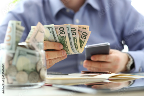 Male hand holding pack of banknotes and cellphone making some calculation planning his future expenses closeup concept