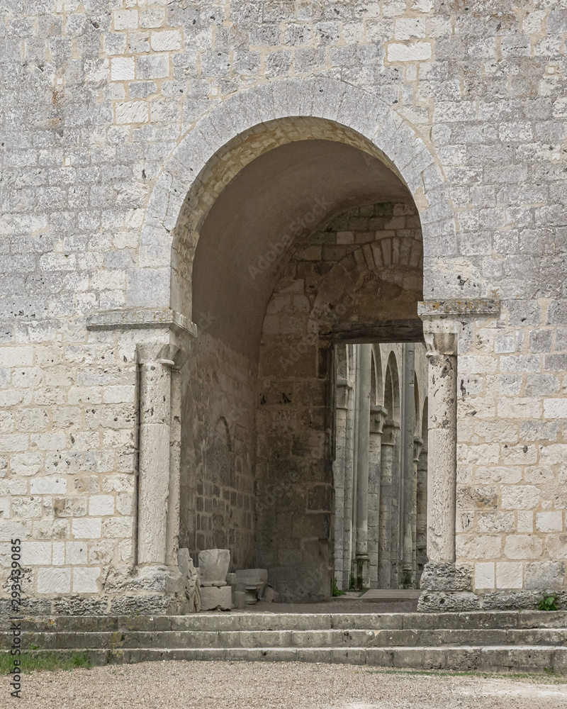White stone wall with arched entryway, with broken sculpture, and columns visible beyond at the ruined 11th century Jumieges Abbey in Normandy France. White stone wall with arched entryway, with broken sculpture, and columns visible beyond at the ruined 11th century Jumieges Abbey in Normandy France.