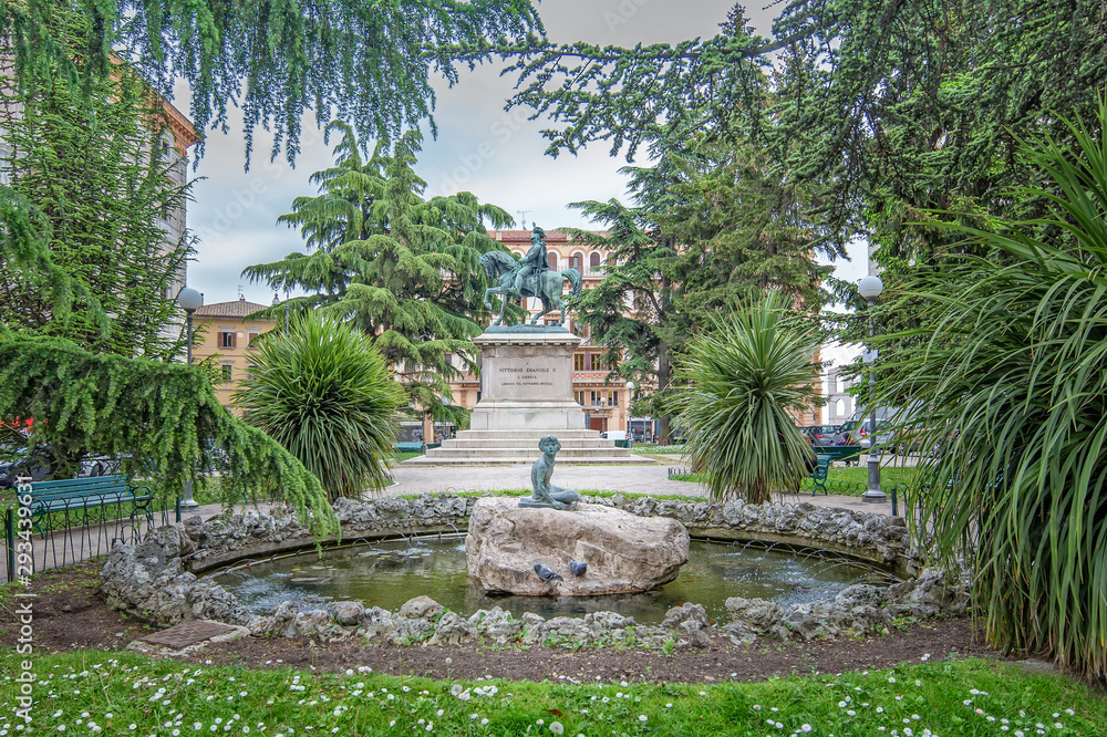 Little oasis at the fountain of Piazza Italia.The gardens, the fountain and in the background the equestrian monument to Vittorio Emanuele II in Piazza Italia, Perugia, Italy