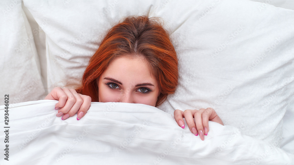 the girl playfully peeping out from under the blankets. the girl playfully peeping out from under the blankets.