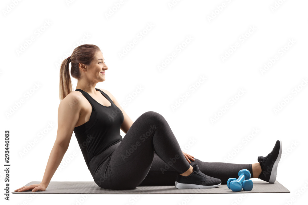 Happy woman sitting on an exercise mat with dumbbells Happy woman sitting on an exercise mat with dumbbells