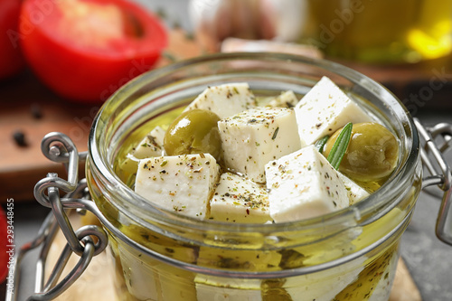 Pickled feta cheese in jar on grey table, closeup