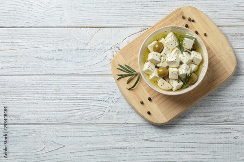 Flat lay composition with pickled feta cheese in bowl on white wooden table, space for text photo