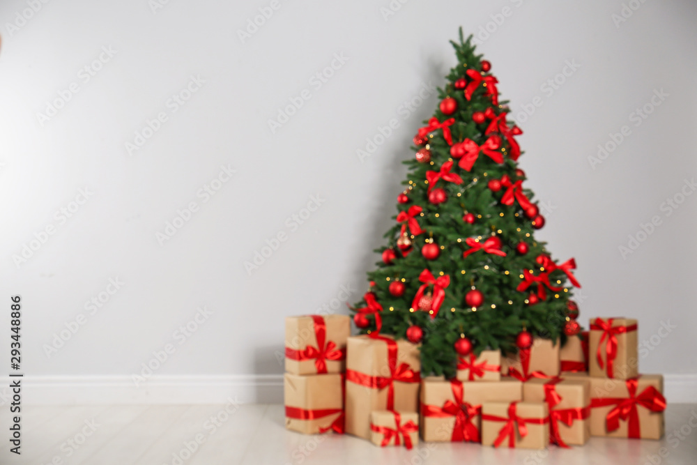 Blurred view of decorated Christmas tree and gift boxes near light wall. Space for text