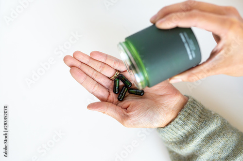 Woman pouring green vitamin supplements in jar