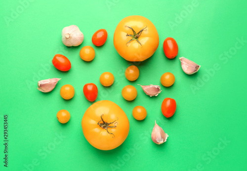 Different fresh tomatoes and garlic on color background