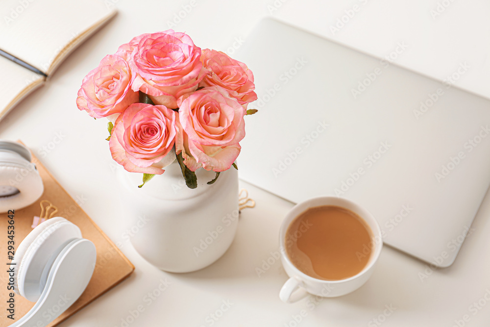 Beautiful rose flowers with laptop, cup of coffee and headphones on white table Beautiful rose flowers with laptop, cup of coffee and headphones on white table