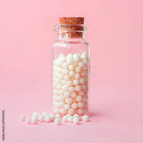 Close-up image of homeopathic globules in glass bottle on pastel pink background. Alternative homeopathy medicine herbs, healthcare and pills concept photo