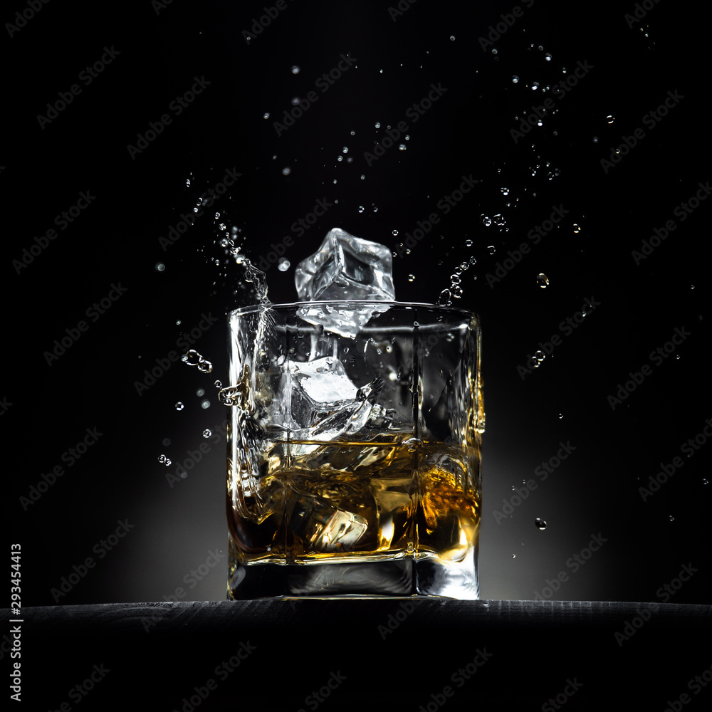 Glass of whiskey with ice cubes falling in it with splashes and drops