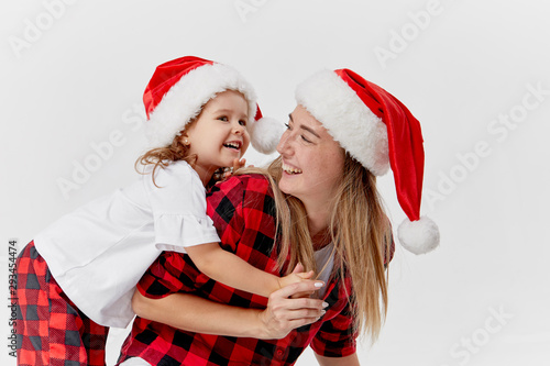 Christmas time. Happy hugging family, mother and daughter, little child playing in Santa hats, isolated on white. New year holiday concept