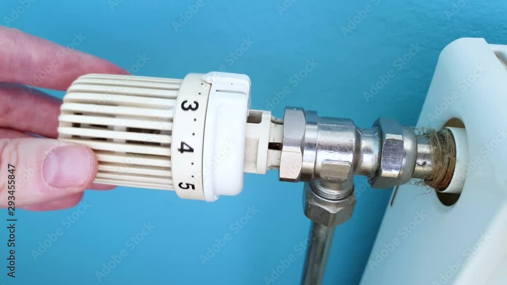 Adjusting and rotating white temperature valve with hand on wall mounted heating water radiator Adjusting and rotating white temperature valve with hand on wall mounted heating water radiator