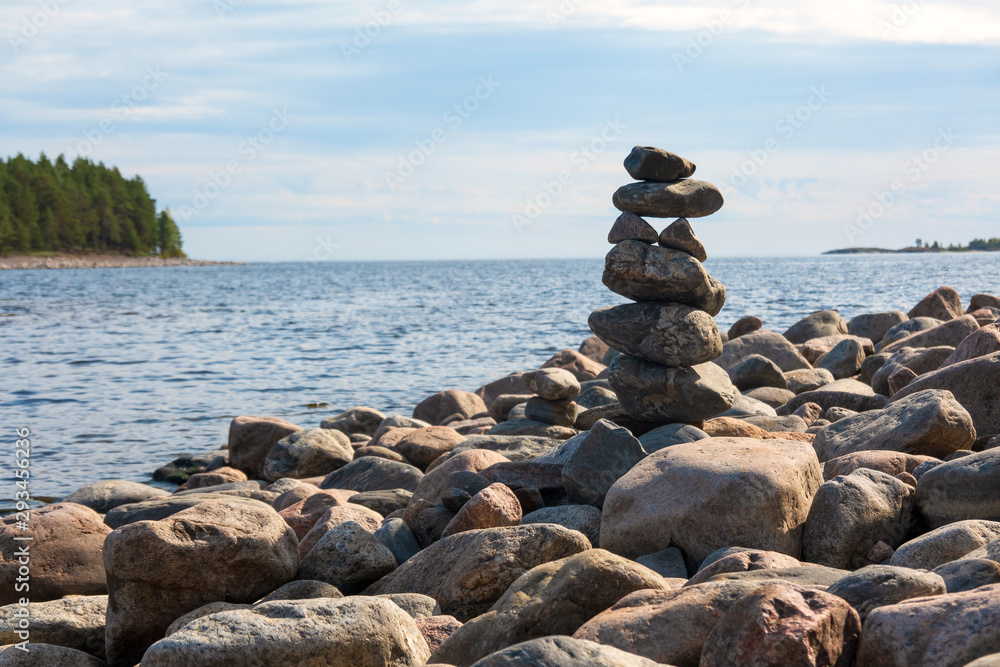 A fragment of the rocky shore of a large lake. On the shore there is a figure made of natural stones. Background. Scenery.