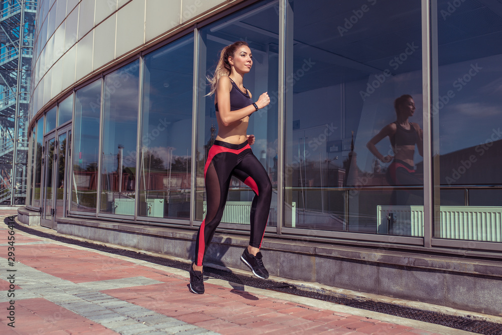 Beautiful girl athlete running jump in training, background glass windows, summer autumn spring in city, free space for motivation text, sportswear, active fitness lifestyle, outdoor sport exercise.