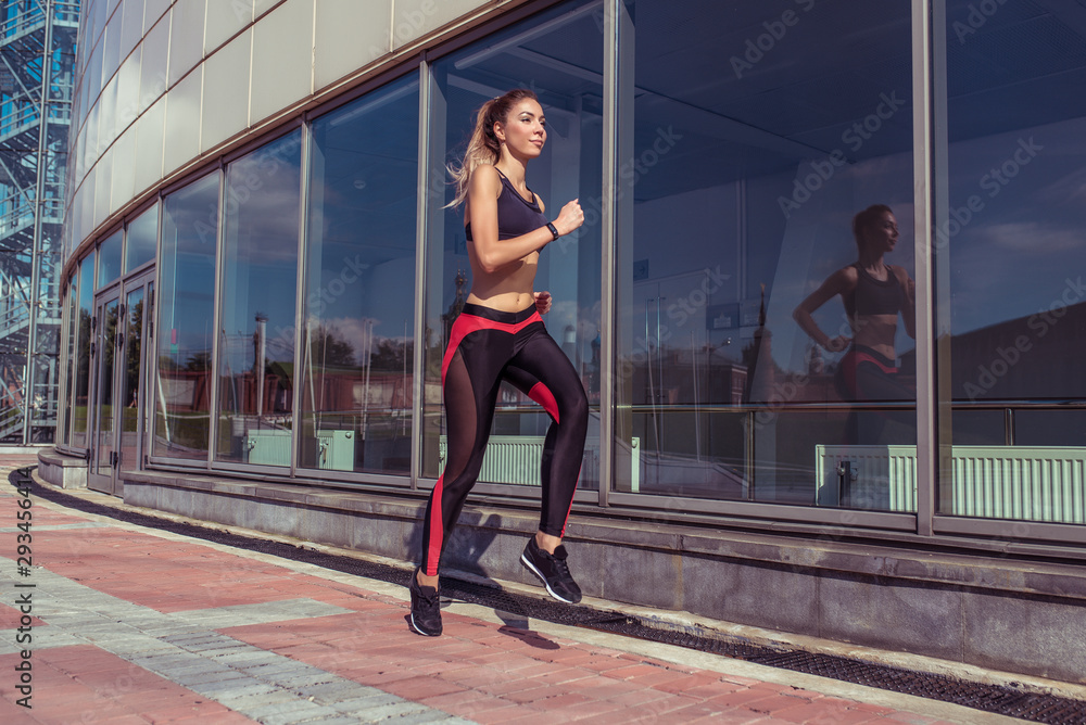 Beautiful girl athlete running jump in training, background glass windows, summer autumn spring in city, free space for motivation text, sportswear, active fitness lifestyle, outdoor sport exercise. Beautiful girl athlete running jump in training, background glass windows, summer autumn spring in city, free space for motivation text, sportswear, active fitness lifestyle, outdoor sport exercise.