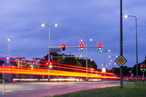 Slow shutter speed night photo of Dutch traffic lights with red brake lights at traffic light intersection with traffic lights that are on green and red