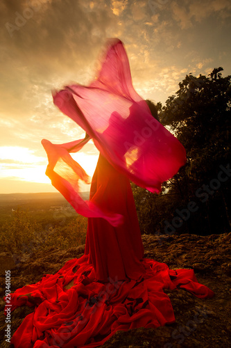 Dancer outdoors, twirling a fans with red fabric on them. photo