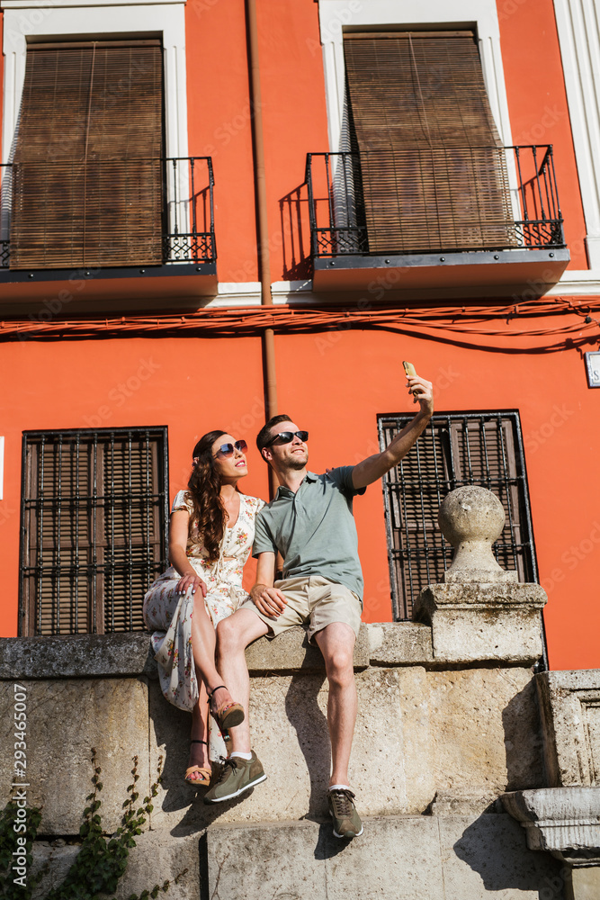 Couple sitting on a wall taking selfie with smartphone, Granada, Spain Couple sitting on a wall taking selfie with smartphone, Granada, Spain