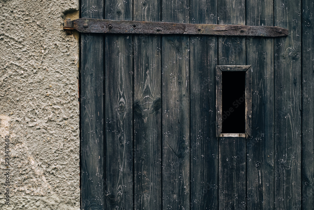 Spooky dark vertical window in rustic ancient textured wood door with rusty metal hinge / Halloween horror concept